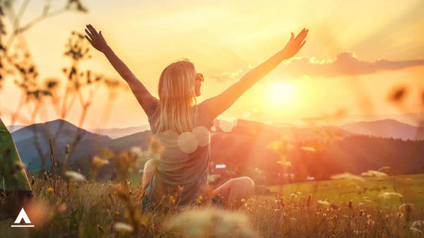 Woman in exercise gear stretching arms out in relief at top of mountain during golden sunset hour, outdoor activities with camping and hiking khyam. Showcasing health benefits of camping.